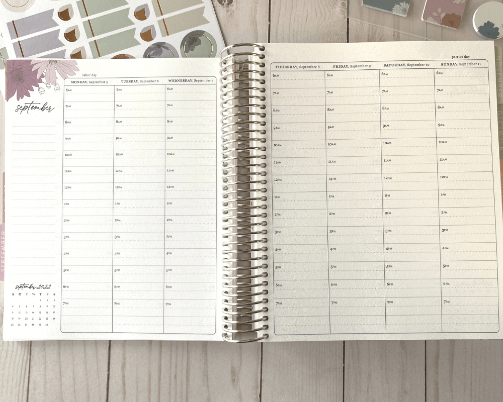 An open Erin Condren weekly life planner in the hourly format on a light wood background. Shows 7 days of the week. and some stickers underneath the planner in the top left corner.